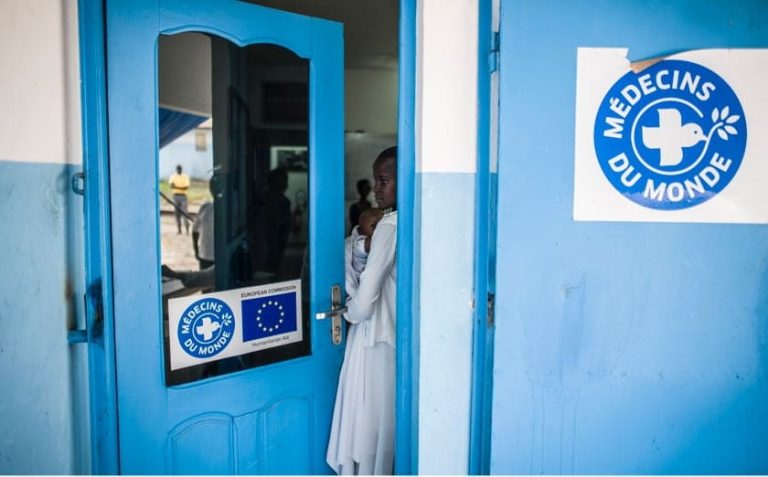 une femme dans l'entrebaillement d'une porte bleu avec logo médecins du monde